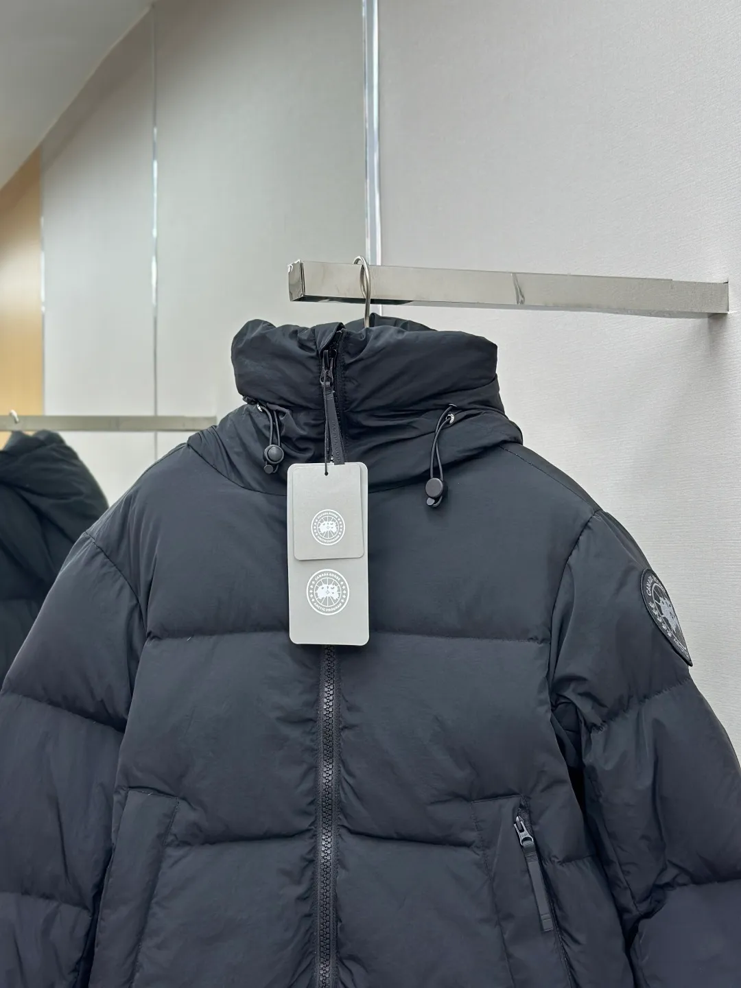 P1010 Canada Goose Black Label Badge Hooded Down Jacket (khaki) The high-quality filling is made of 90 national standard high-quality white duck down, selected high-loft velvet, weighing 240g, light and warm, with excellent temperature locking performance and good resilience. The fabric is woven with 400T high-count yarn. After special water-repellent treatment, the surface forms a lotus leaf effect - raindrops will slide down like beads, and snow particles will fall off when touched. The tear resistance reaches 200N (approximately 20kg load-bearing), the light gray matte texture breaks the stereotype of "outdoor clothing = hardcore", and the soft luster presents a high-end matte effect under urban neon lights, seamlessly switching scenes from ski resorts to CBD office buildings. The ribbon is woven with polyester as the base, and the brand letters are decorated on the ribbon through high-precision computer embroidery. The edges of the pattern are clear, the stitches are fine and even, and multiple layers of embroidery thread are stacked to enhance the three-dimensional effect. Precision thread reinforcement prevents linting and ensures the fluffy and resilient elasticity lasts as new. The embedded cuffs are three-dimensionally woven to form a "wavy" elastic structure, which forms natural folds when fitting the wrist, increasing the contact area with the skin, thus improving the windproof effect. At the same time, micro-velvet treatment is added to the inside of the cuffs, which feels like a second layer of skin and avoids friction on the skin from metal zippers or hard fabrics. Size:S-M-L-XL